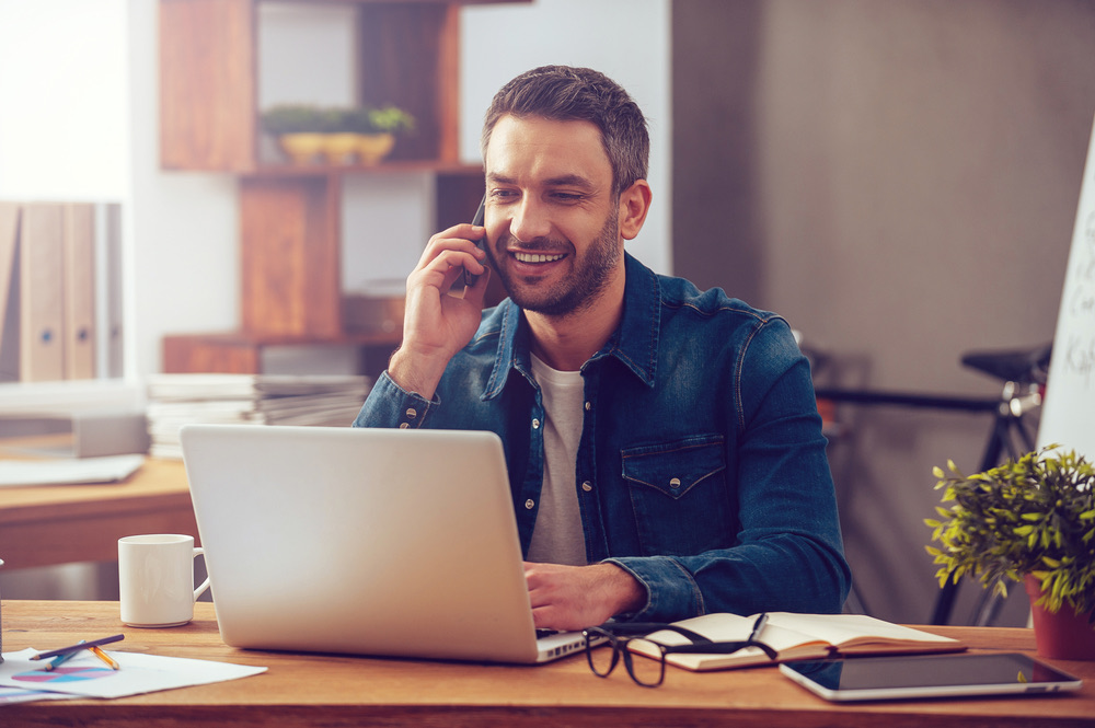 A man on a phone call while working at a laptop